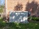 A residential backup power generator sits on a lawn in front of a brick home. A tree is casting a shadow on the generator and brick wall.