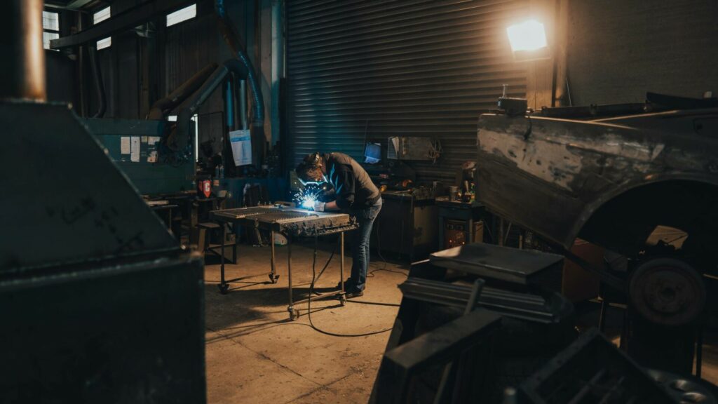 A metalworking business owner working on a project with their welding equipment and protective gear.