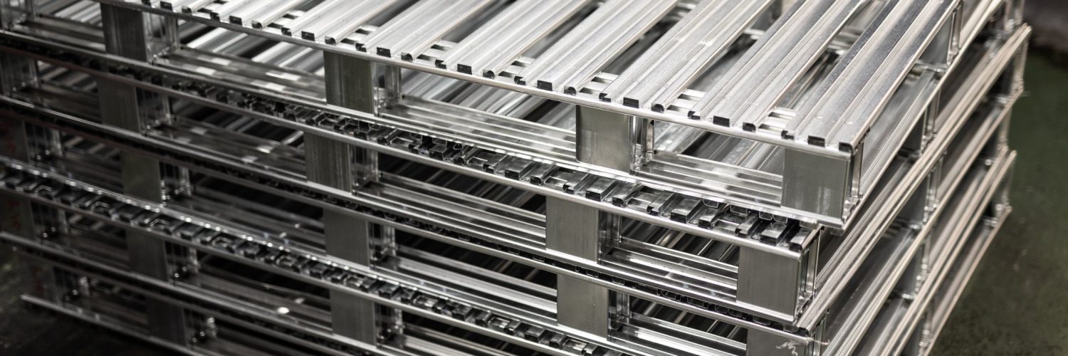 A close-up of five large aluminum metal pallets stacked together on a black concrete floor in a building.