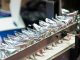 A machine holds several shiny, silver plastic pouches lined up in a row and secured by a metal arm bar.