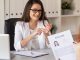 A manager grins at a job candidate who sits in front of her. The candidate holds a copy of their resume.