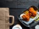 An assortment of fast food offerings in to-go or delivery packaging sitting on a black wooden table.