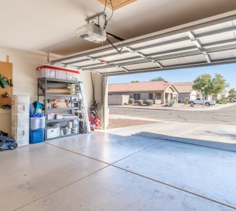 A garage with the exterior door open. There are various tools and boxes stacked against the garage wall.