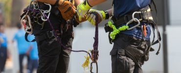 A close-up of two people wearing safety gloves and safety harnesses with ropes and multiple carabiners attached.