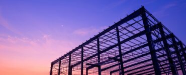 The steel structure of a partially built industrial warehouse, with the sunset behind the framework.