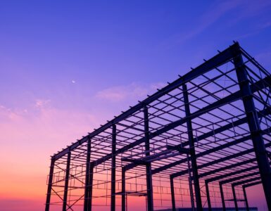 The steel structure of a partially built industrial warehouse, with the sunset behind the framework.