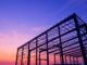 The steel structure of a partially built industrial warehouse, with the sunset behind the framework.