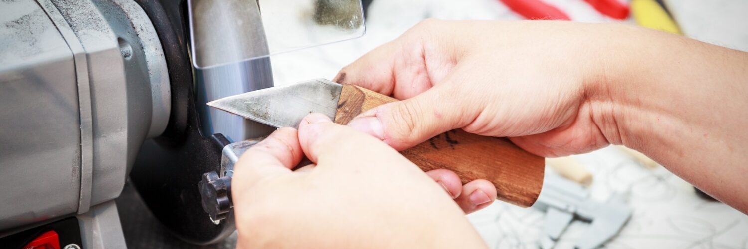 a close-up of a metal cutter being sharpened on a grinding machine, with sparks and machinery visible nearby.